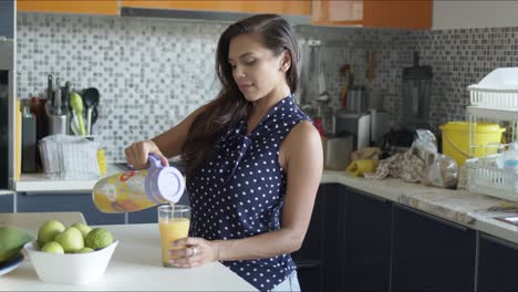 Charming-happy-woman-sipping-fresh-orange-juice-standing-in-kitchen