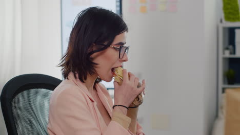 Entrepreneur-woman-eating-tasty-sandwich-having-work-break-working-in-business-company