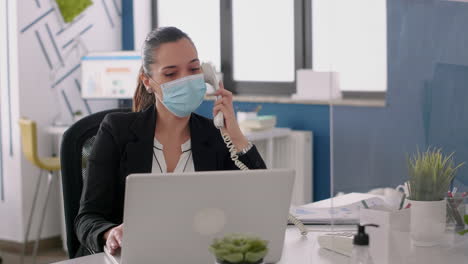 Freelancer-with-face-mask-talking-at-phone-while-checking-financial-reports