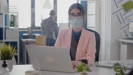 Portrait-of-business-woman-with-protection-face-mask-working-on-laptop-computer