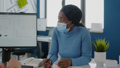 African-employee-with-face-mask-explaning-project-to-invalid-coworker