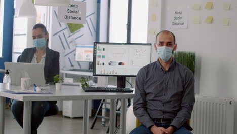 Portrait-of-businessman-with-protective-face-mask-while-sitting-in-startup-corporate-office