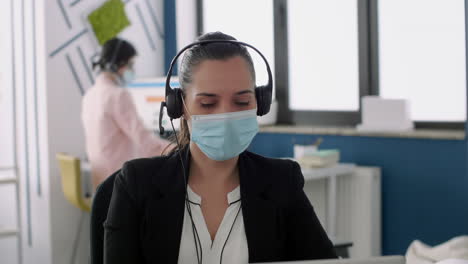 Worker-wearing-medical-face-mask-and-headphone-discussing-with-partners-into-microphone