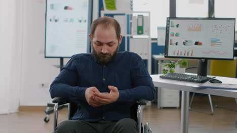 Disabled-entrepreneur-holding-smartphone-texting-during-work-time
