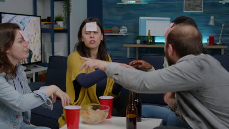 Mixed-race-friends-playing-Guess-who-game-with-sticky-papers-attached-on-forehead