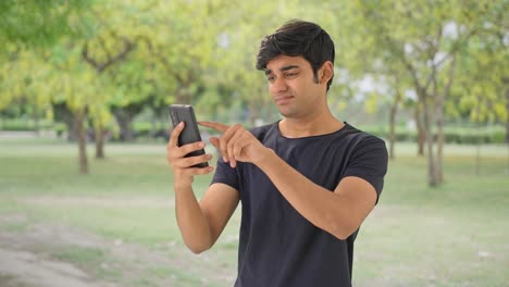 Bored-Indian-man-scrolling-phone-in-park