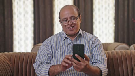 Glücklicher-Indischer-Alter-Mann,-Der-Durch-Sein-Mobiltelefon-Scrollt