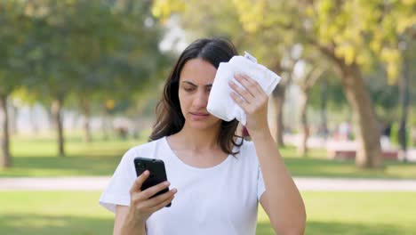 Indian-woman-using-phone-while-cleaning-the-sweat-in-a-park-in-morning