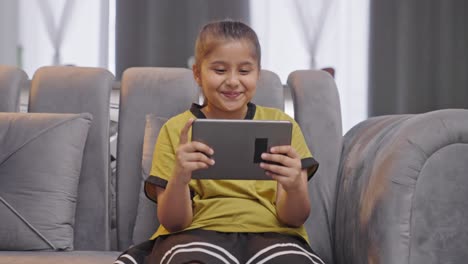 Happy-Indian-kid-girl-watching-videos-on-tablet