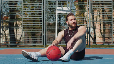 Hombre-Libanés-Atlético-Cansado-En-Ropa-Deportiva-Relajándose-Después-De-Jugar-Baloncesto,-Escuchando-Música