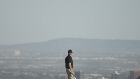 Wide-tilt-down-view-of-a-golfer-walking-on-a-golf-course-with-mountains-and-a-city-in-the-background