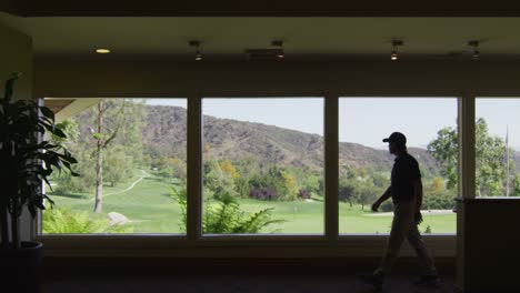 A-golfer-inside-a-country-club-with-a-golf-course-visible-through-the-windows