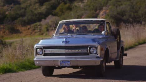 A-group-of-friends-in-a-blue-pickup-truck-drive-on-a-rural-road
