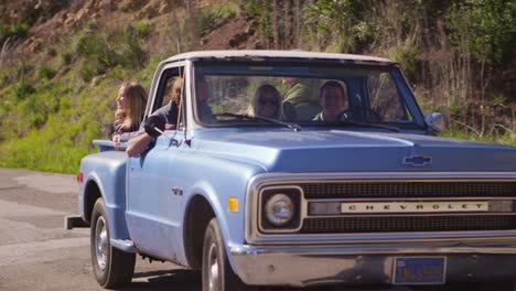 A-group-of-friends-in-a-blue-pickup-truck-drive-on-a-rural-road-1