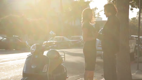 A-man-runs-down-the-street-and-greets-a-woman-getting-onto-her-Vespa-motorbike