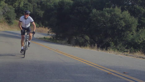 Traveling-slow-motion-shot-of-mountain-bike-rider-pedaling-uphill-along-a-highway