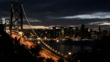 Die-Oakland-Bay-Bridge-Von-San-Francisco-Wird-Heller,-Wenn-Die-Dunkelheit-über-Der-Skyline-Der-Stadt-Hereinbricht