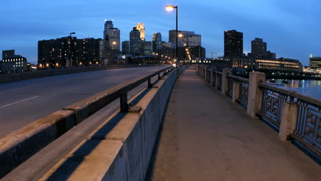 Fußgänger-Und-Fahrzeuge-überqueren-Eine-Brücke-In-Der-Innenstadt-Von-Minneapolis,-Während-Sich-Der-Abendhimmel-Zur-Nacht-Verdunkelt