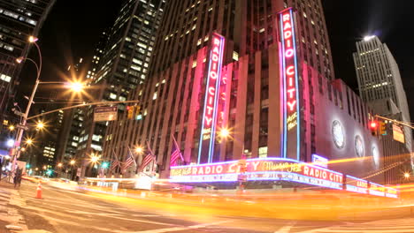 Rosa-Und-Goldene-Lichter-Verschmelzen-Zu-Einer-Beschleunigten-Aufnahme-Des-Verkehrs,-Der-Nachts-Vor-Der-Radio-City-Music-Hall-Vorbeifährt