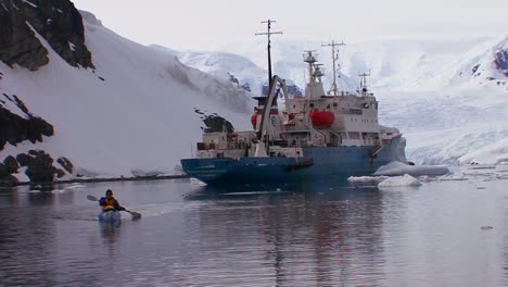 A-man-kayaks-near-a-ocean-research-vessel-in-Antarctica