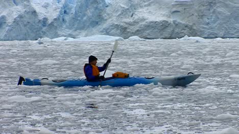 A-man-paddles-a-kayak-in-the-Arctic-or-Antarctic-with-many-icebergs-nearby
