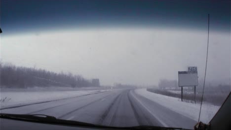 A-POV-shot-through-a-car-windshield-traveling-on-a-snowy-road-in-winter