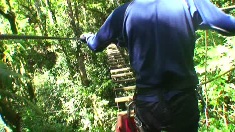 A-POV-shot-of-a-man-crossing-a-rickety-footbridge-over-a-jungle-ravine
