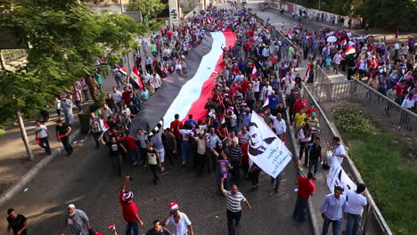 Los-Manifestantes-Marchan-Y-Llevan-Una-Gran-Bandera-En-El-Cairo,-Egipto