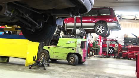 An-Auto-Repair-Shop-With-Cars-On-Lifts-And-Mechanics-Walking-In-The-Background