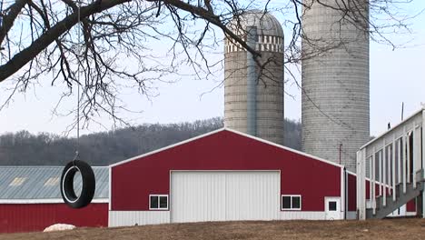 A-Tire-Swing-Hangs-From-A-Tree-With-A-Bright-Red-Barn-And-Silos-In-The-Background