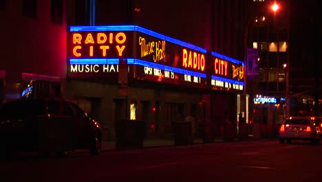 Los-Coches-Pasan-Por-La-Carpa-Del-Salón-Musical-De-Radio-City-Brillantemente-Iluminada-Por-La-Noche