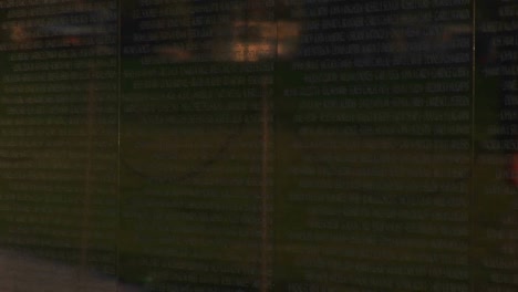 View-Moves-Upward-From-Small-Flags-Edging-The-Vietnam-War-Memorial-Wall-To-A-Larger-Flag-Reflected-Over-Names-On-The-Wall
