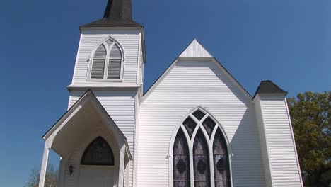 The-White-Clapboard-Exterior-Of-An-Old-Country-Church-Is-Set-Against-A-Blue-Sky-In-This-Panning-Shot