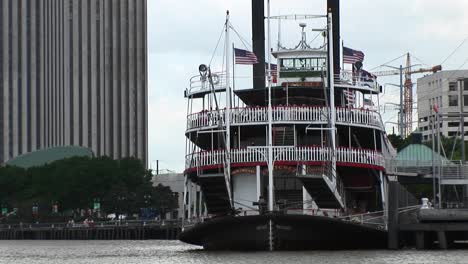 The-Mississippi-River-Flows-Around-A-Paddleboat-Full-Of-Tourists-As-It-Sits-Docked-In-New-Orleans