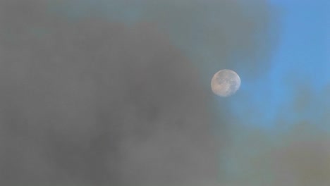 Lange-Aufnahme-Dunkler-Rauchwolken,-Die-Sich-Auflösen,-Um-Den-Mond-Am-Blauen-Himmel-Zu-Enthüllen