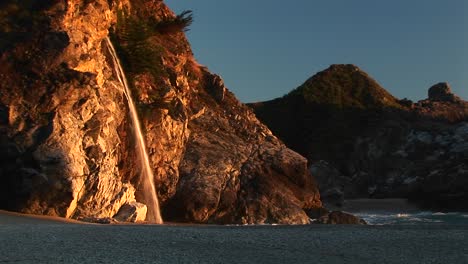Mittlere-Aufnahme-Eines-Wasserfalls,-Der-Auf-Einen-Abgelegenen-Strand-Im-Julia-Pfeiffer-Burns-State-Park-Entlang-Des-Kalifornischen-Pazifischen-Ozeans-Stürzt