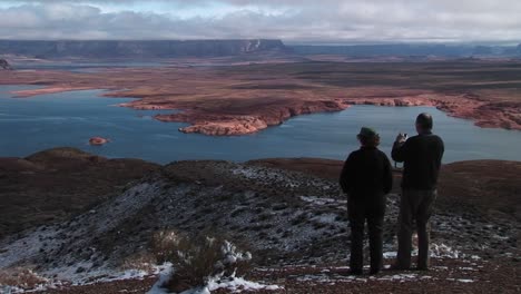 Mediumshot-De-Una-Pareja-De-Pie-Sobre-Una-Zona-De-Nieve-Mirando-Por-Encima-Del-Lago-Powell-Arizona