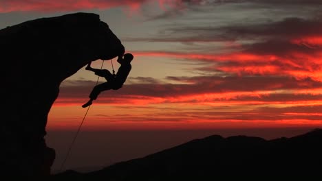 A-Man-Climbs-A-Rugged-Peak-In-Silhouette-At-Sunset