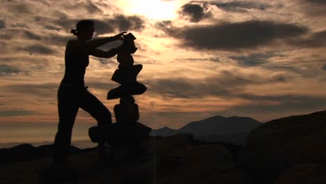 Mediumshot-Of-A-Silhouetted-Woman-Stacking-Rocks-On-A-Mountaintop