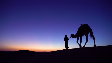 Eine-Klassische-Reiseabenteueraufnahme-Eines-Mannes,-Der-In-Silhouette-Ein-Kamel-über-Eine-Düne-Führt