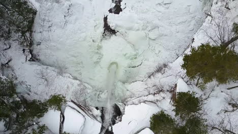 Beautiful-winter-aerial-shot-flying-over-a-high-waterfall-in-a-frozen-landscape
