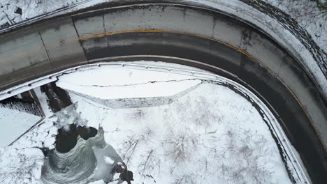 An-aerial-POV-perspective-looking-straight-down-on-a-highway-winding-through-a-frozen-wilderness