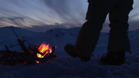 Closeup-of-a-man's-legs-beside-a-campfire-in-winter
