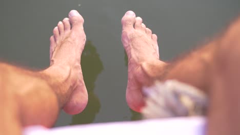 Mann-Mit-Baumelnden-Beinen-über-Wasser