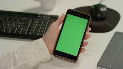 Cu-Frau-Am-Schreibtisch-Hält-Telefon-Mit-Grünem-Bildschirm