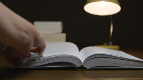 Pan-of-Female-Hand-Turning-Page-of-Book-at-Night