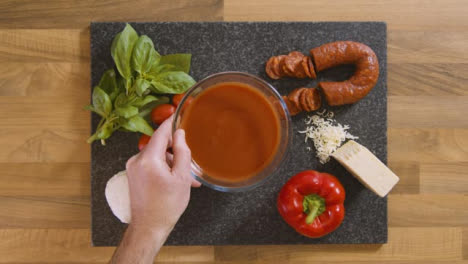 Top-View-Male-Puts-Bowl-of-Tomato-Sauce-on-Worktop