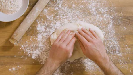 Top-View-Male-Flattens-Dough-on-Flour-Covered-Worktop