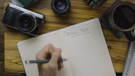 Man-Writing-Dream-Trip-In-His-Notebook-on-Coffee-Table