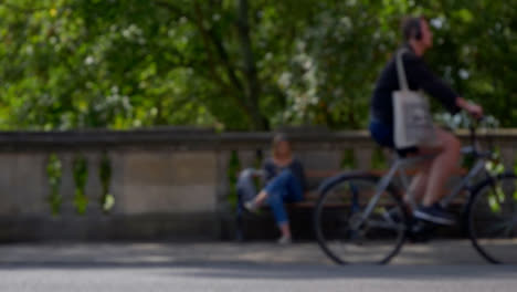 Defocused-Shot-of-People-and-Traffic-Moving-In-Front-of-Woman-Sat-On-Bench-02